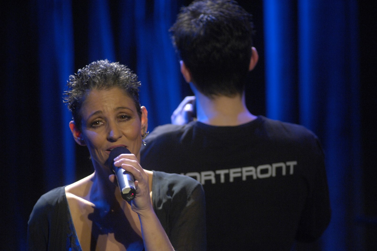 Sandra Kreisler singt, hinter ihr Roger Stein im Wortfront-Shirt vor blauem Vorhang