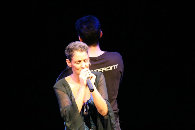 Sandra Kreisler singt mit geschlossenen Augen, hinter ihr Roger Stein im Wortfront-Shirt mit dem Rücken zum Publikum