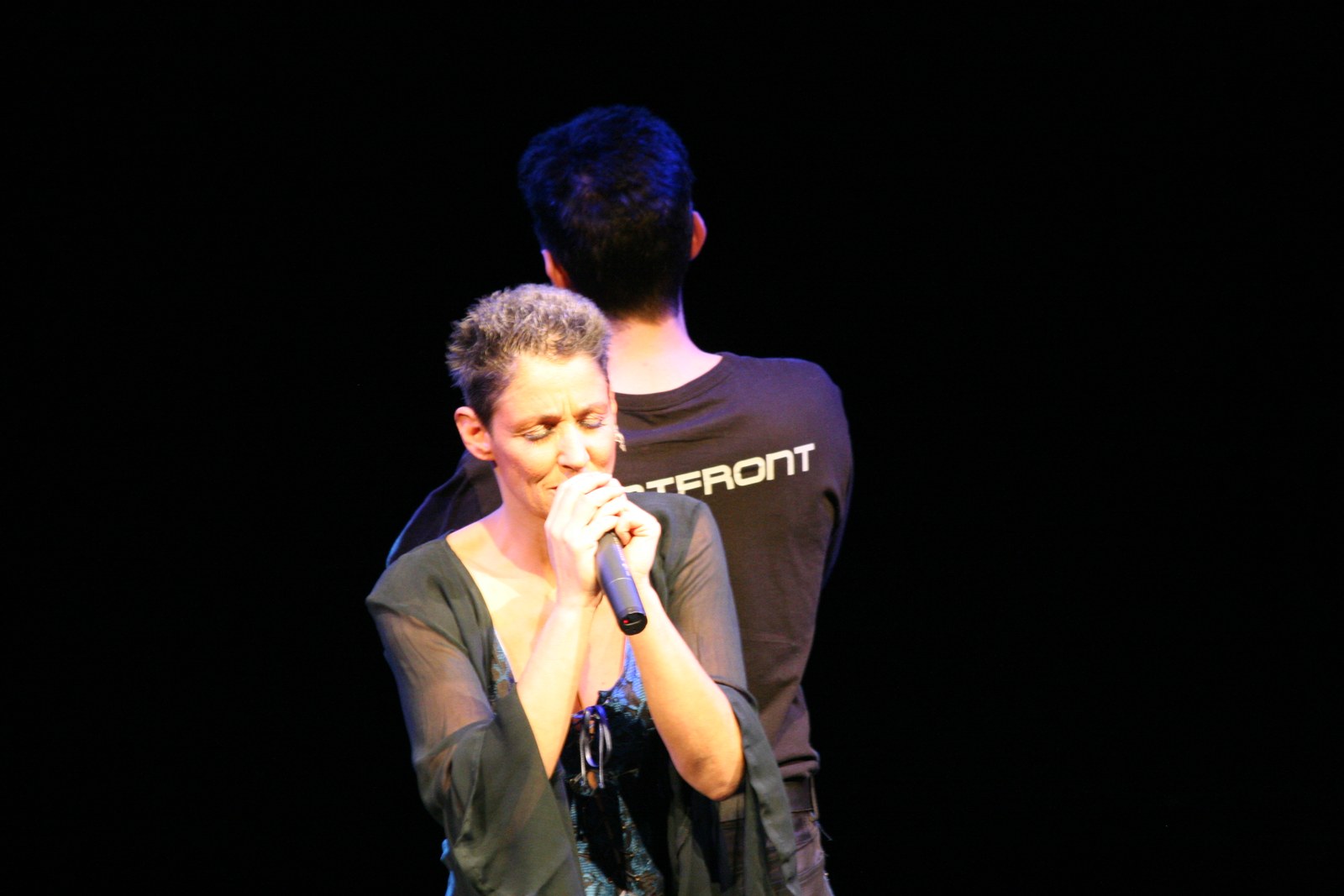 Sandra Kreisler singt mit geschlossenen Augen, hinter ihr Roger Stein im Wortfront-Shirt mit dem Rücken zum Publikum