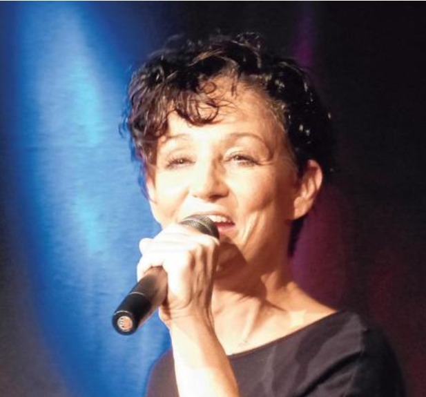 Sandra Kreisler singt lächelnd ins Mikrofon vor blauem Licht