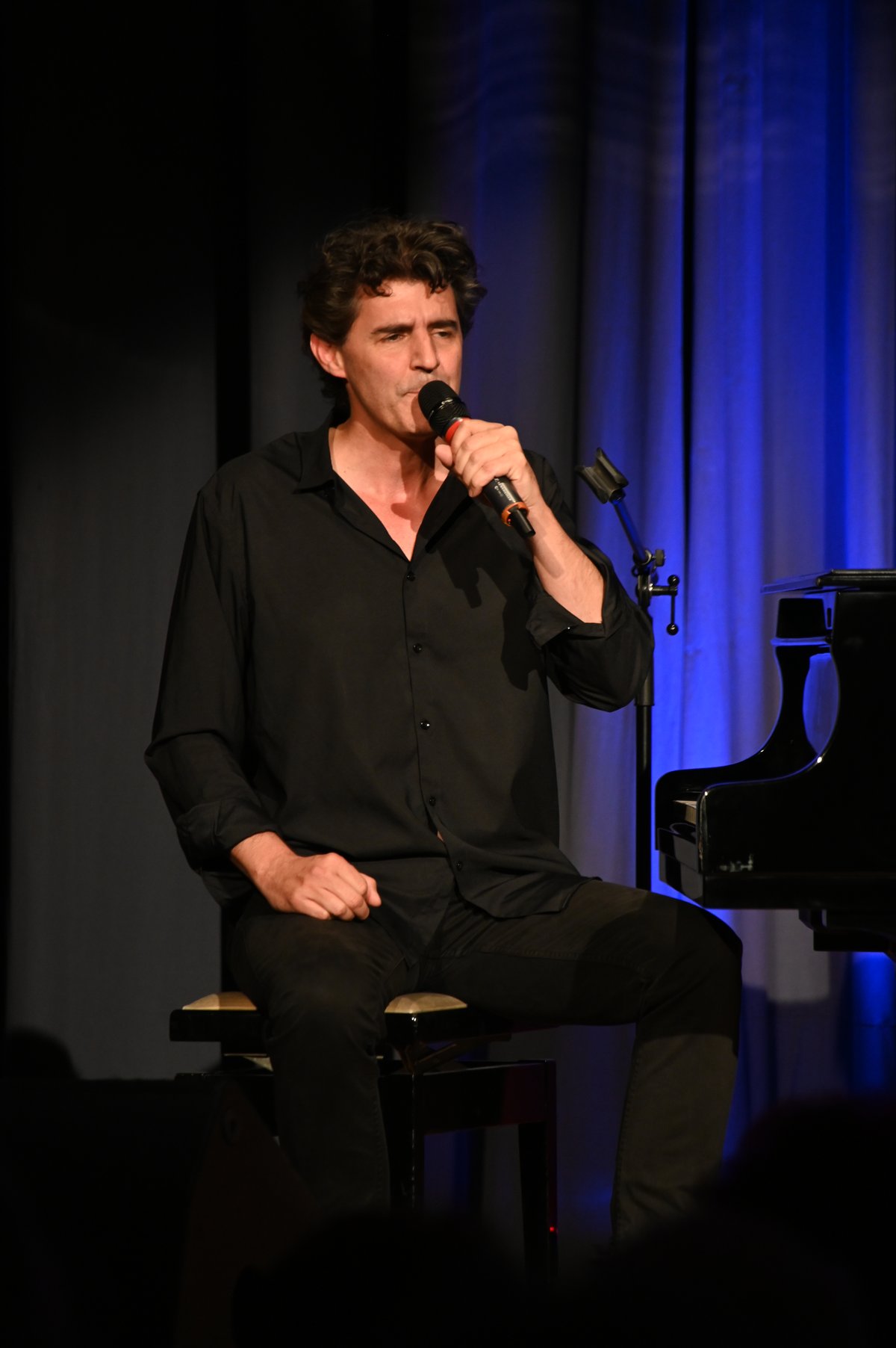 Roger Stein sitzt auf dem Klavierhocker und singt ins Mikrofon