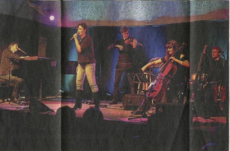 Wortfront mit Band auf der Bühne im Bürgerhaus: Roger Stein am Flügel, Sandra Kreisler mit Mikrofon, dahinter Geige, Cello und Schlagzeug