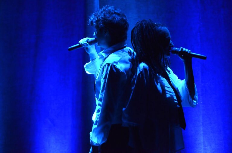 Roger Stein und Sandra Kreisler stehen Rücken an Rücken auf der Bühne und singen in blauem Licht in ihre Mikrofone